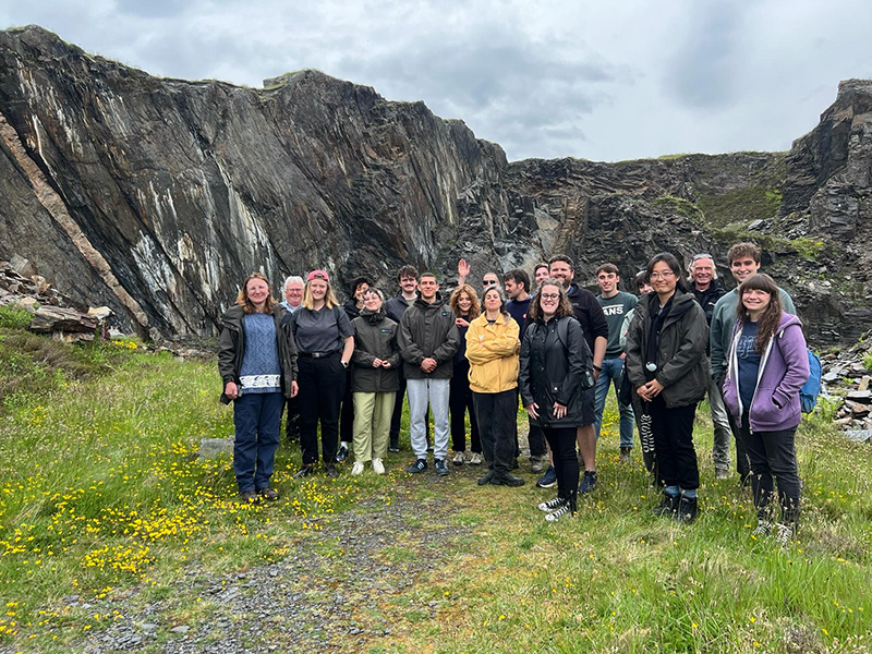 A large group of people standing smiling in front of a dis-used slate quarry