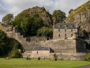 A complex of historic stone castle buildings in excellent condition, with slate roofs and sash and case windows. They are nestled within a rocky crag.