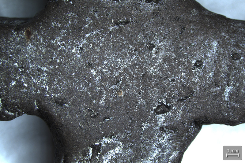 A close up of an old, grey cross which has lots of little white marks all over it