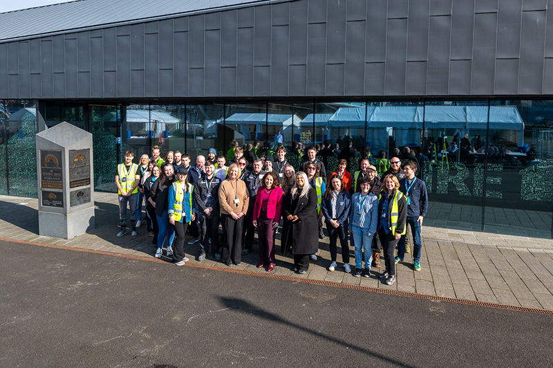 A large group of around 50 people standing together smiling outside the Engine Shed building