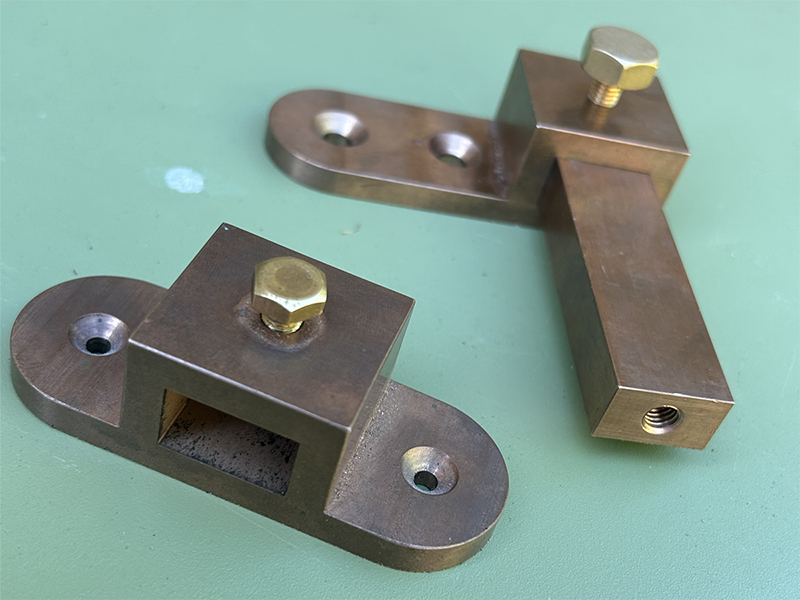 Two bronze fixtures, with holes for screws routed into them and a bolt in each