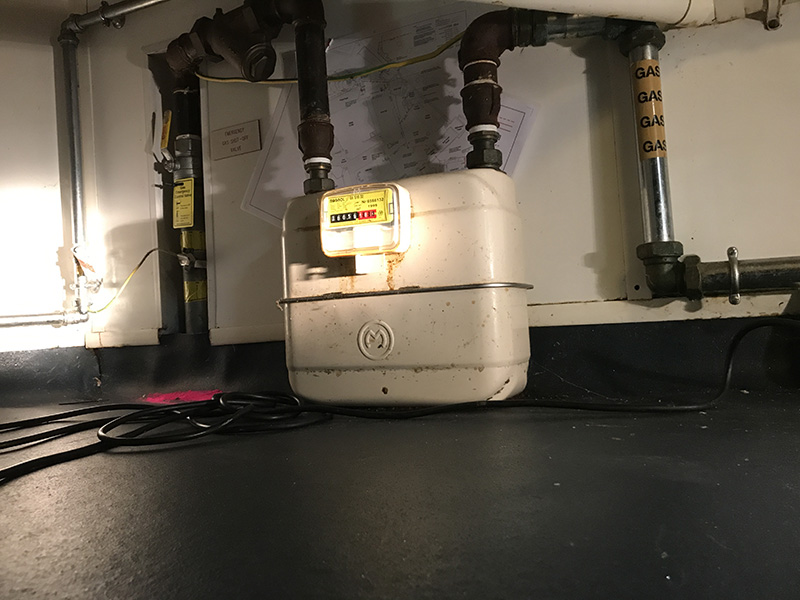 A gas metre on the floor with two large pipes connecting into it