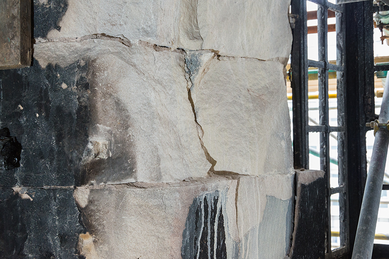 A stone wall that has some black sections and some white sections, damaged by fire. The original stone colour and texture is completely gone.