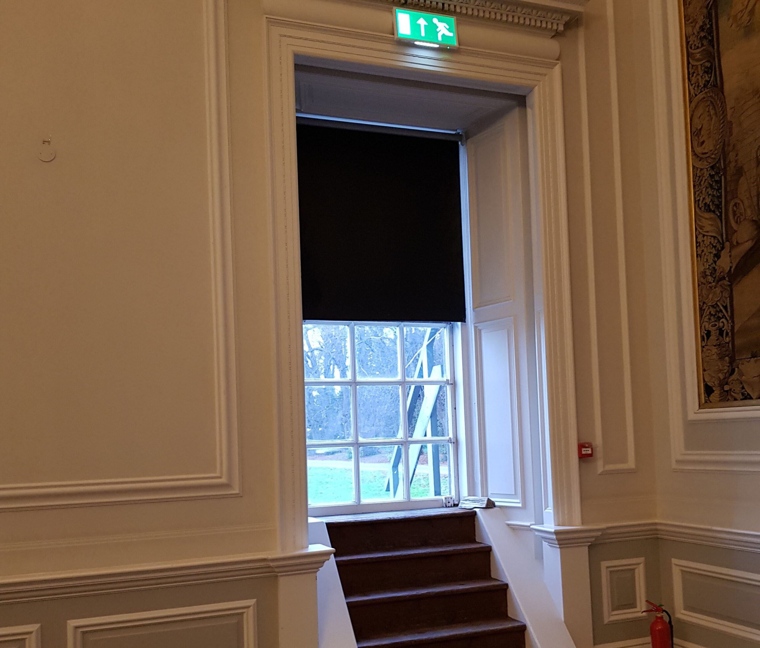 A small staircase leading up to a window that has been transformed into a fire escape. A green fire exit sign is above the window.