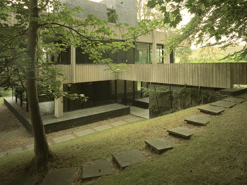 An angular, concrete building with many floor-to-ceiling glass windows, in a rural area