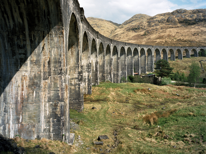 A large concrete viaduct made up of many tall arches, stretching across the countryside with hills in the background