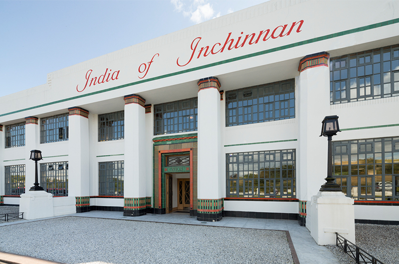A white shop front with grey crittal-style windows and colorful, decorative mosaics on large columns.