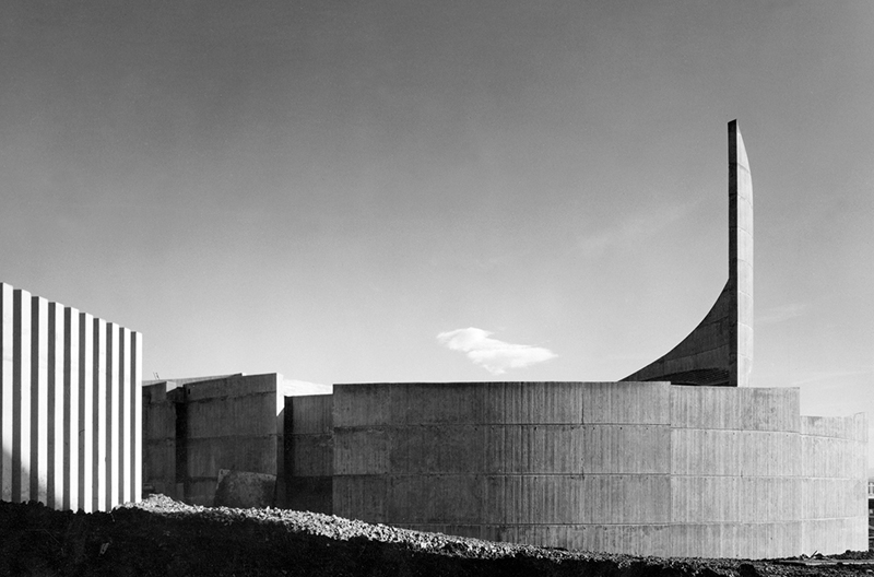 A circular concrete building with a large, circular 'fin' protruding up round the edge of the structure
