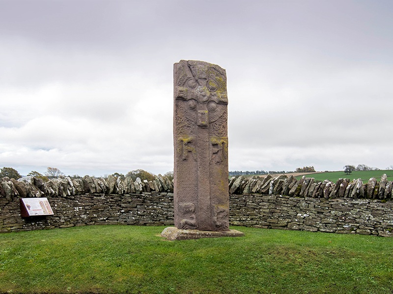 A tall standing stone in a field, with a cross carved into it