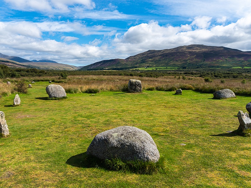 A circle of small boulders in a field, with hills in the background