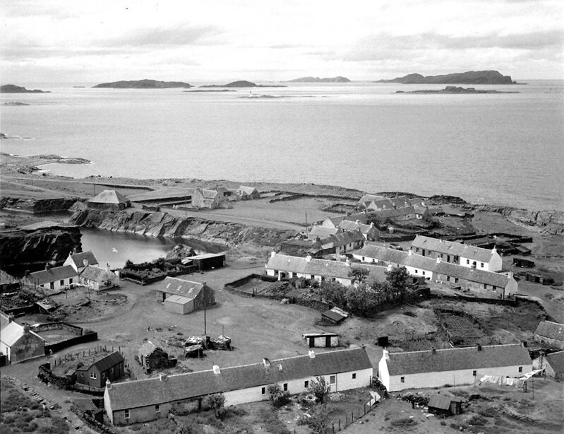 Single-storey cottages with slate roofs surrounding a quarry filled with water, on the edge of the sea.