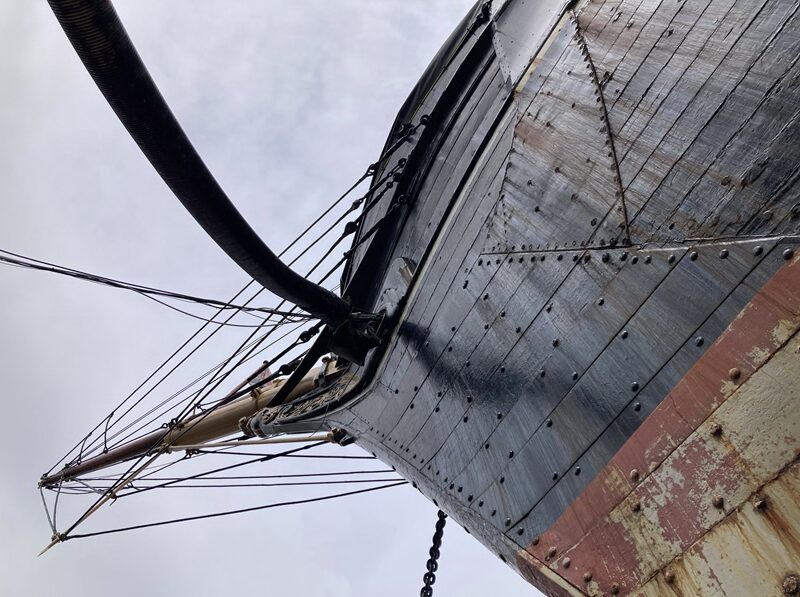 Low-angle view of a traditional sailing ship's bow with rigging, black hull and weathered timber details.