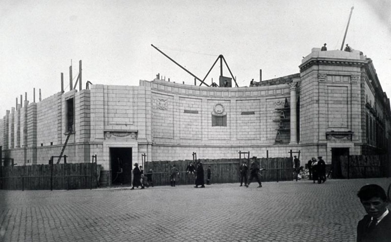 People building a large stone building. You can see the framework at the back of the walls as they build towards it.