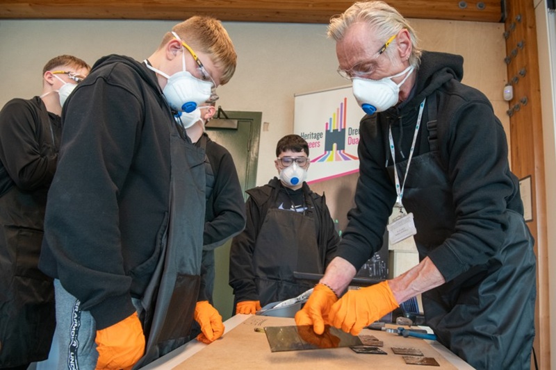 A man working with a group of school pupils on some pieces of stained glass.