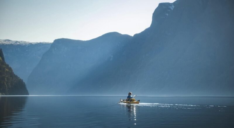 A person kayaking on a lake surrounded by mountains.